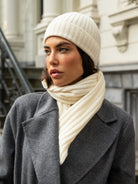 Woman wearing a gray coat, ivory cashmere knit beanie, and scarf in an urban setting.