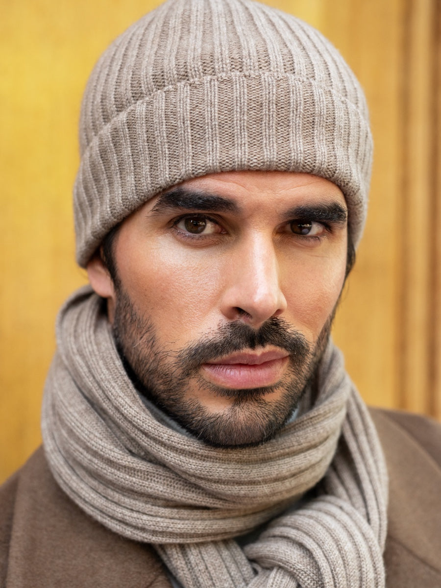 Man wearing a brown cashmere knit beanie and scarf against a yellow background