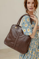 Woman holding a brown leather handbag against a neutral background