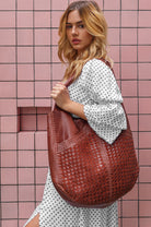 Woman holding a brown woven handbag against a pink tiled wall