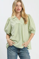 Model wearing a sage and white gingham blouse with an open collared neckline, puff sleeves, and a relaxed fit paired with blue jeans-AVAH