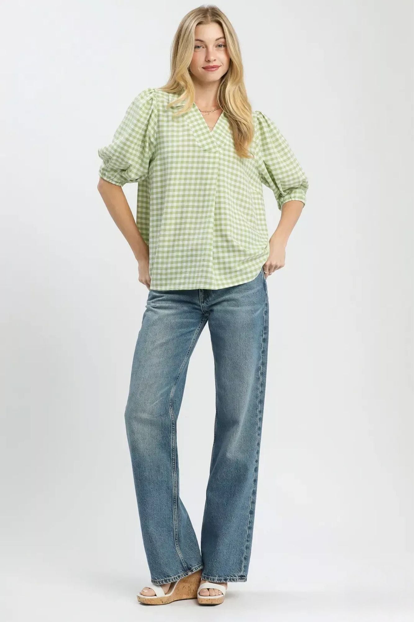 Model wearing a sage and white gingham blouse with an open collared neckline, puff sleeves, and a relaxed fit paired with blue jeans-AVAH