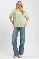 Model wearing a sage and white gingham blouse with an open collared neckline, puff sleeves, and a relaxed fit paired with blue jeans-AVAH