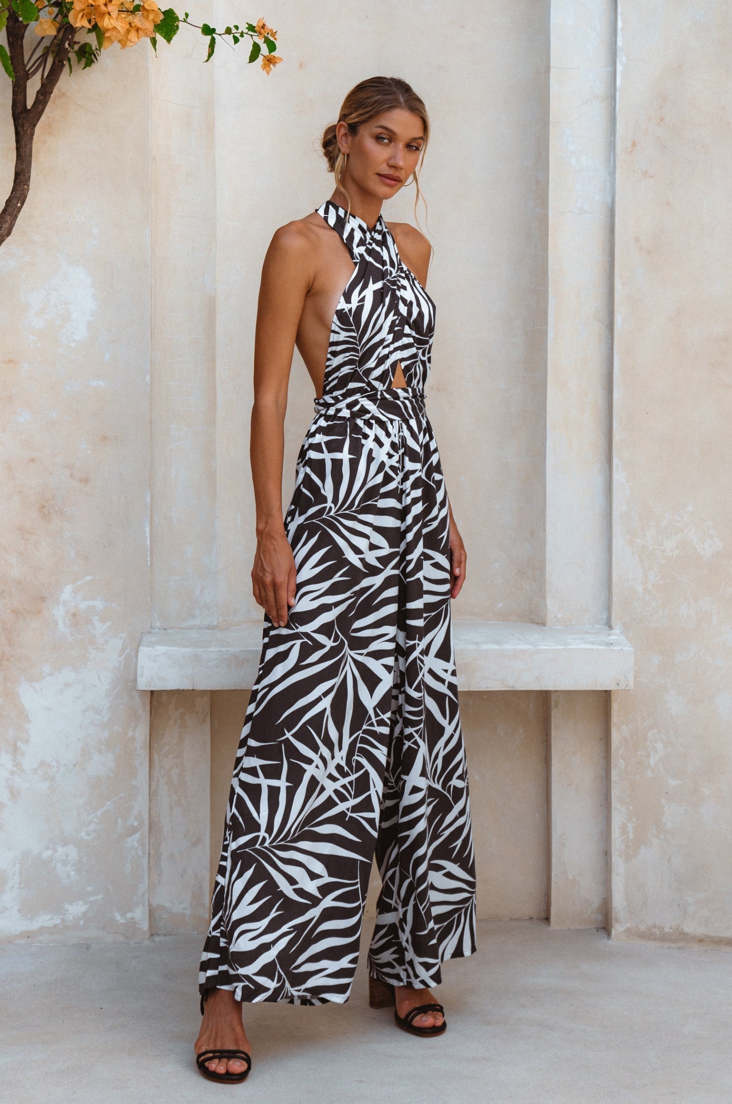 Woman wearing a black and white patterned jumpsuit standing against a light-colored wall, 3/4 view.