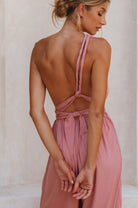 Woman wearing a pink jumpsuit showing the unique ties on the open back with an open back against a neutral, background