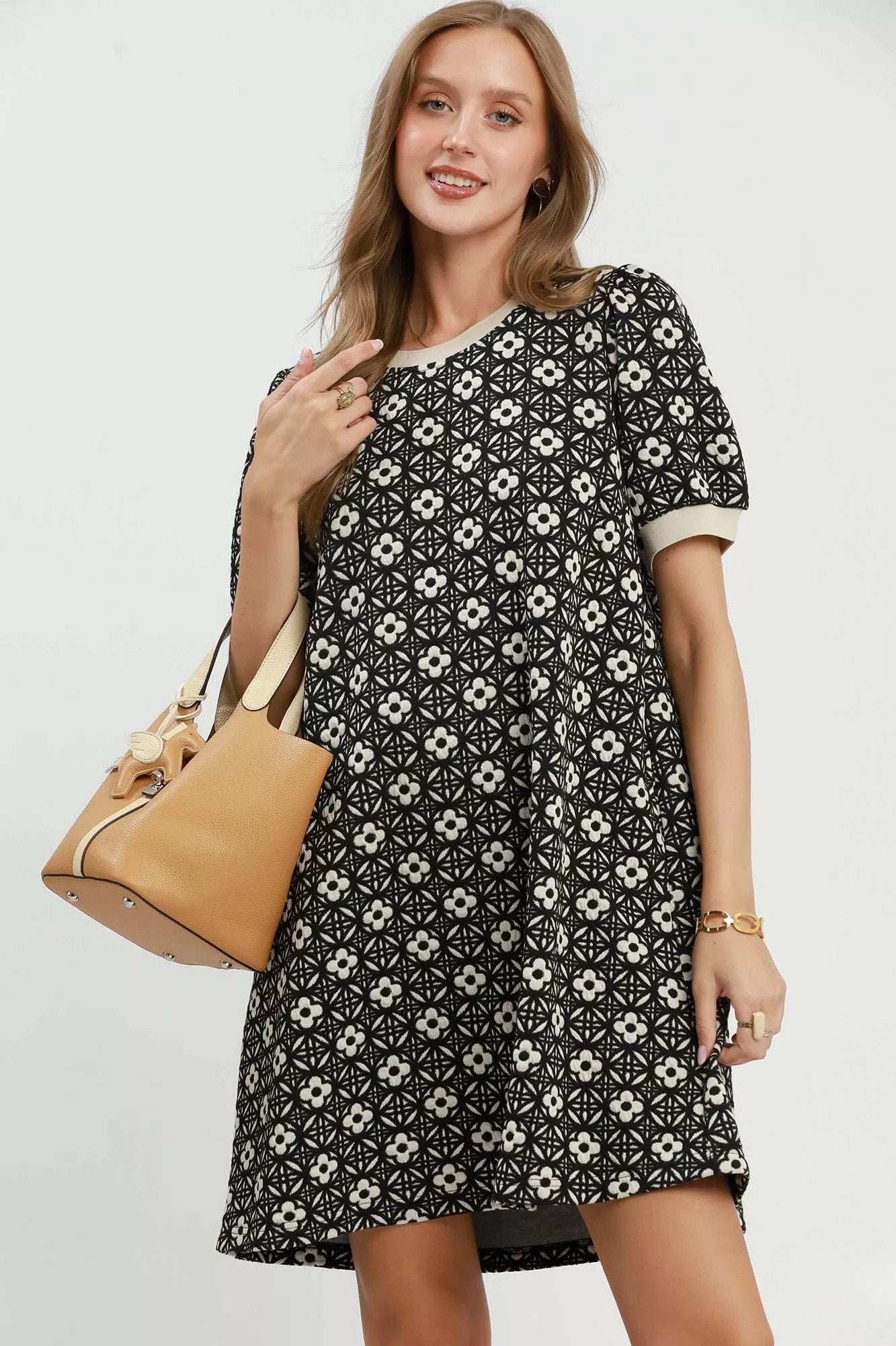 Woman wearing a black floral knit swing dress with short puff sleeves, contrast trim, side pockets, and a relaxed silhouette .