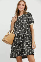 Woman wearing a black floral knit swing dress with short puff sleeves, contrast trim, side pockets, and a relaxed silhouette .