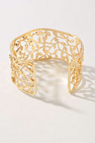 A gold-toned open cuff bracelet with an intricate leaf filigree pattern, displayed on a clean white surface with soft shadows.