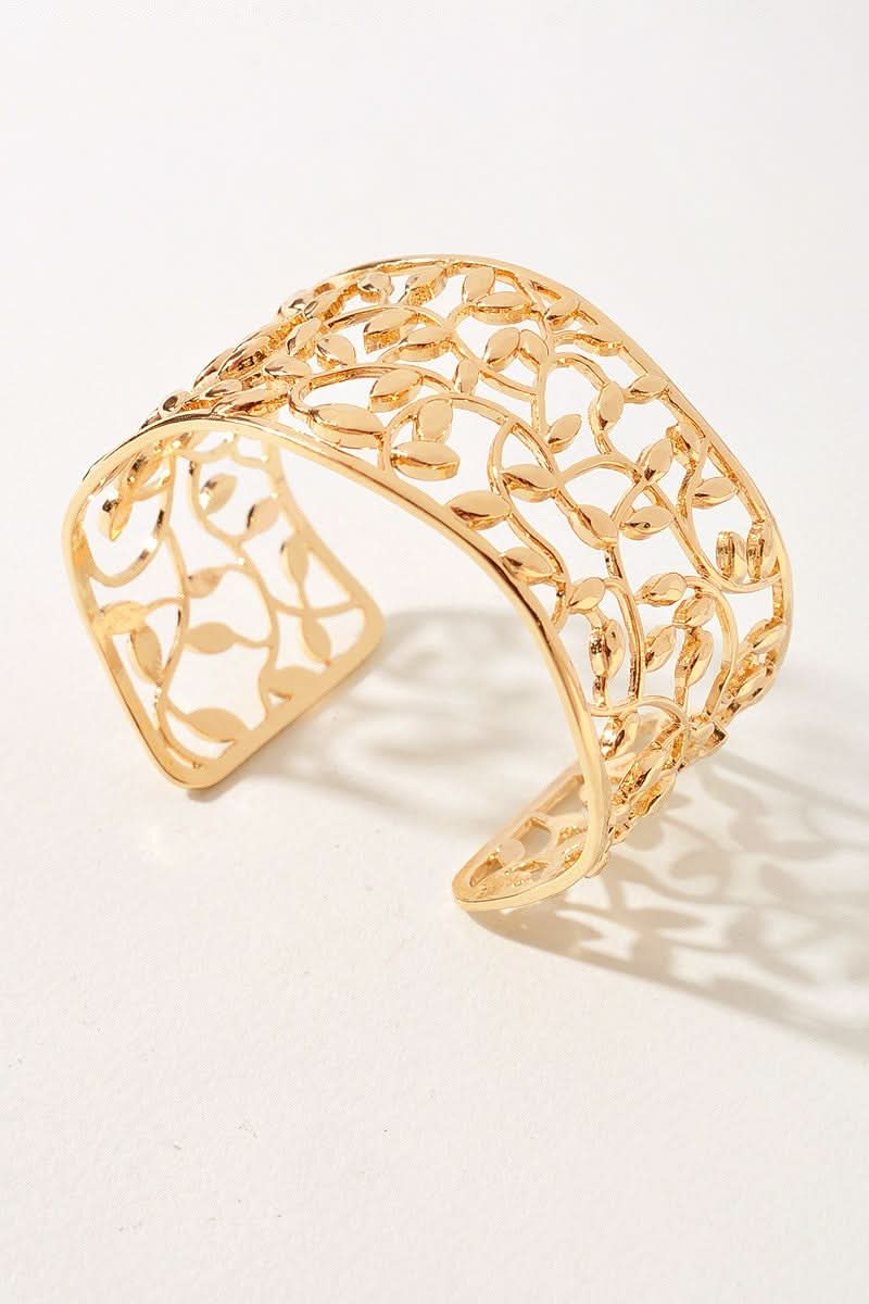 A gold-toned openwork cuff bracelet with a leafy filigree pattern, photographed on a clean white background with a soft shadow.