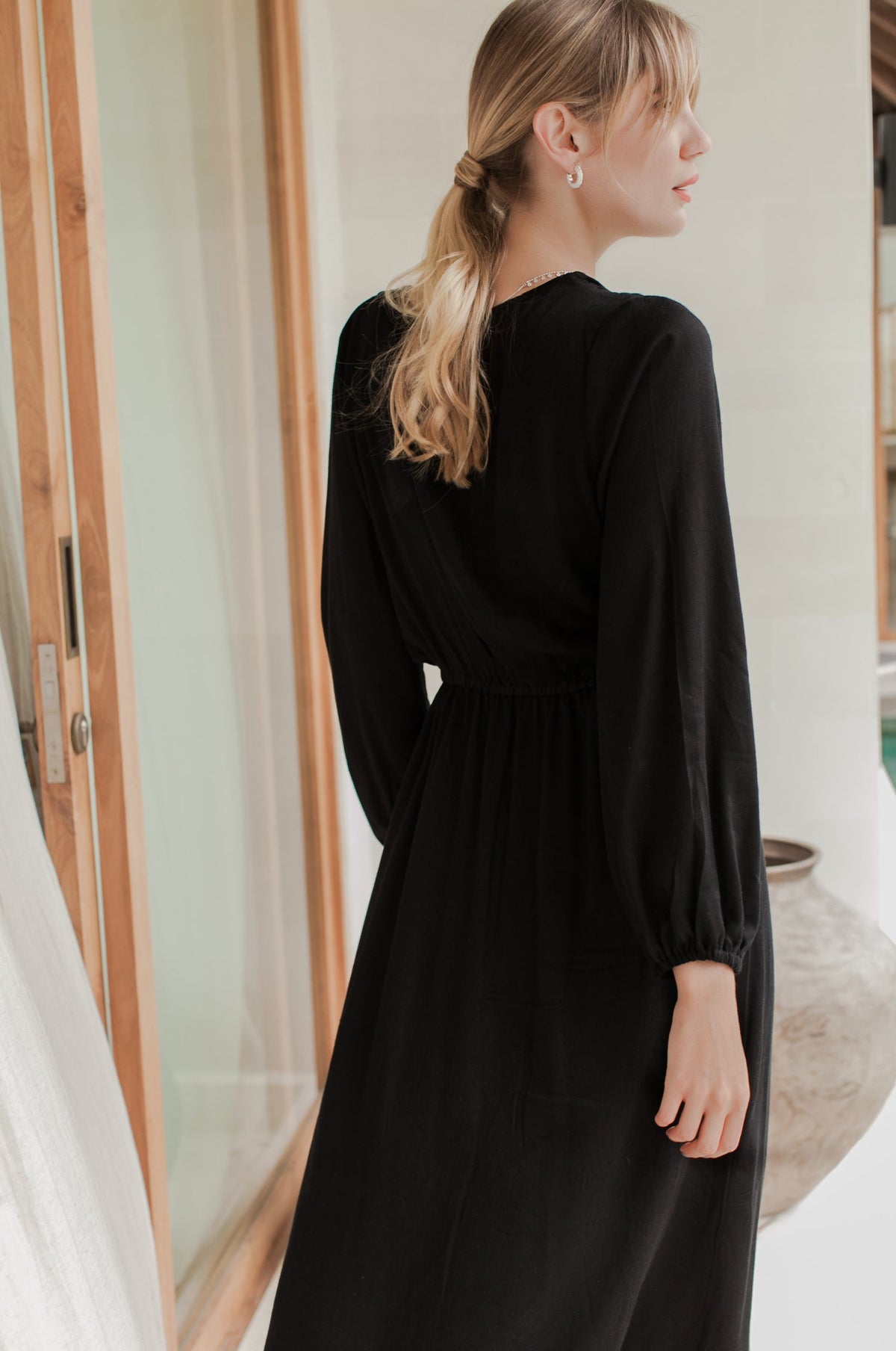 Woman wearing a black dress standing indoors with a neutral background