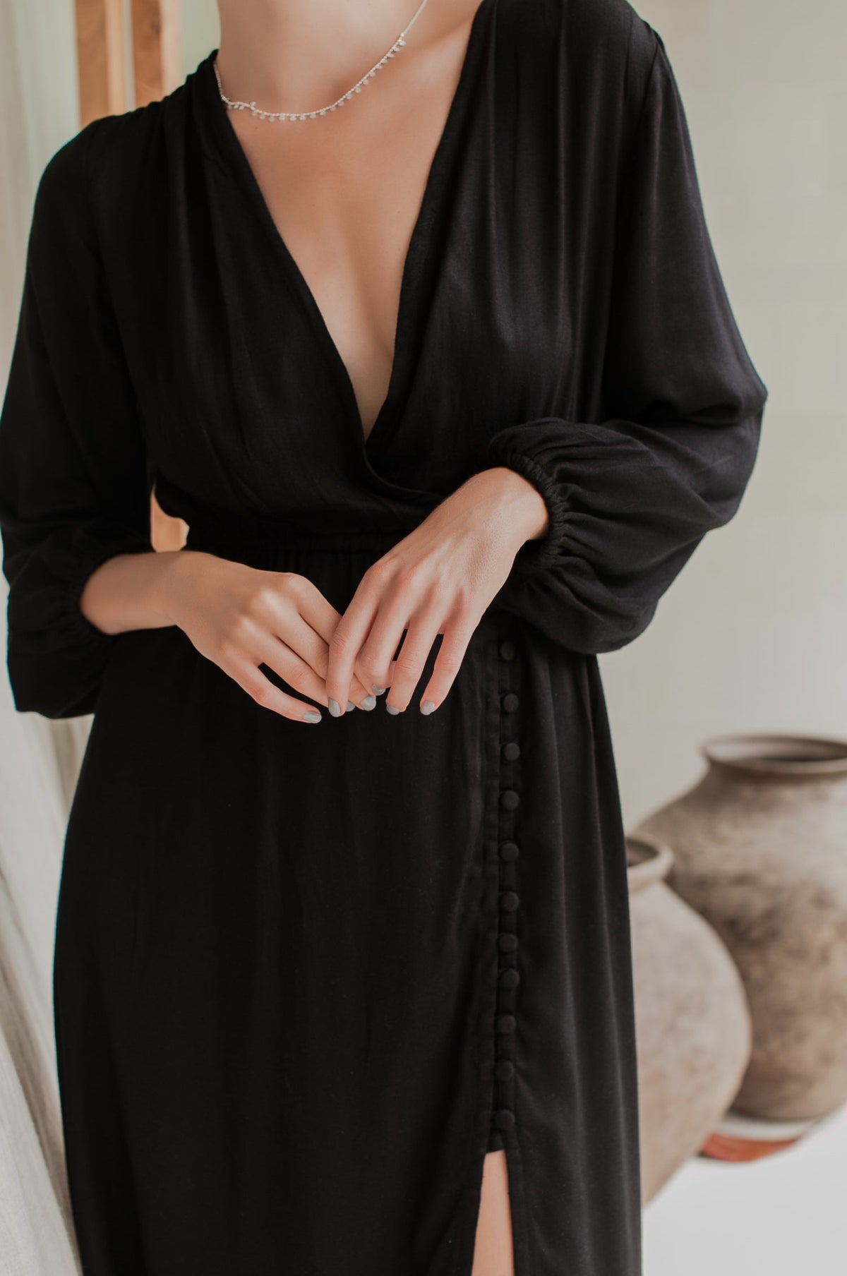 Person wearing a black dress with long sleeves and a deep neckline, standing against a neutral background.