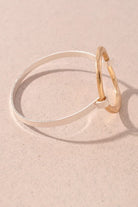 A minimalist two-tone bracelet featuring a thin silver band and a textured gold hoop, resting on a textured beige surface.