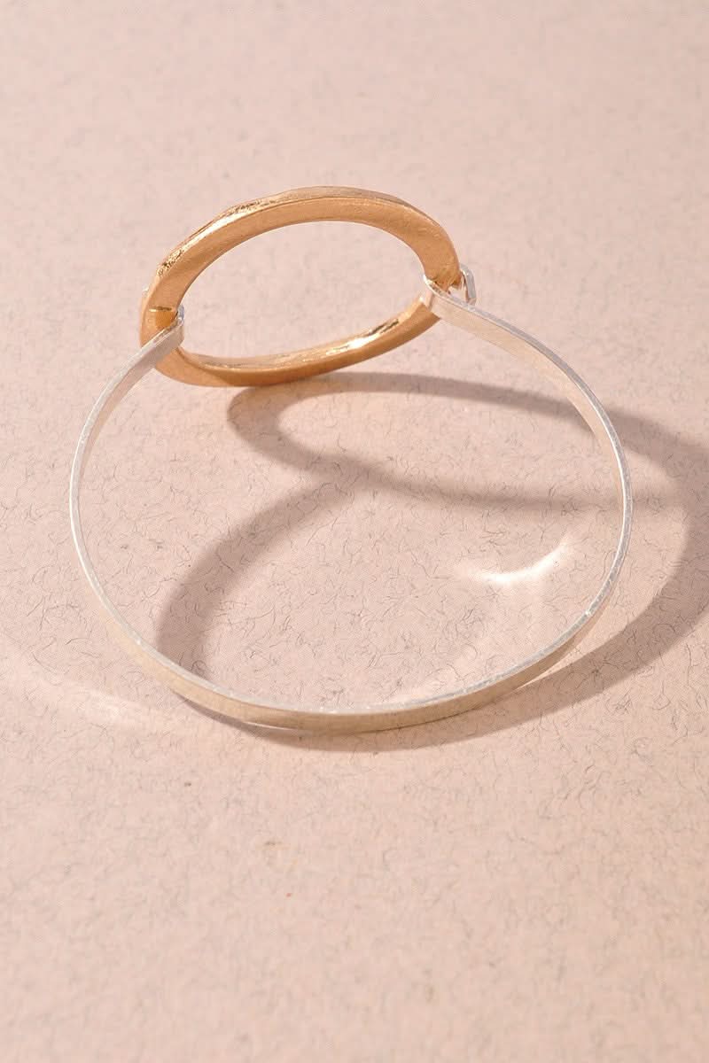 A minimalist gold bracelet with a clear glass or acrylic circular band, photographed on a textured beige surface with a soft shadow.