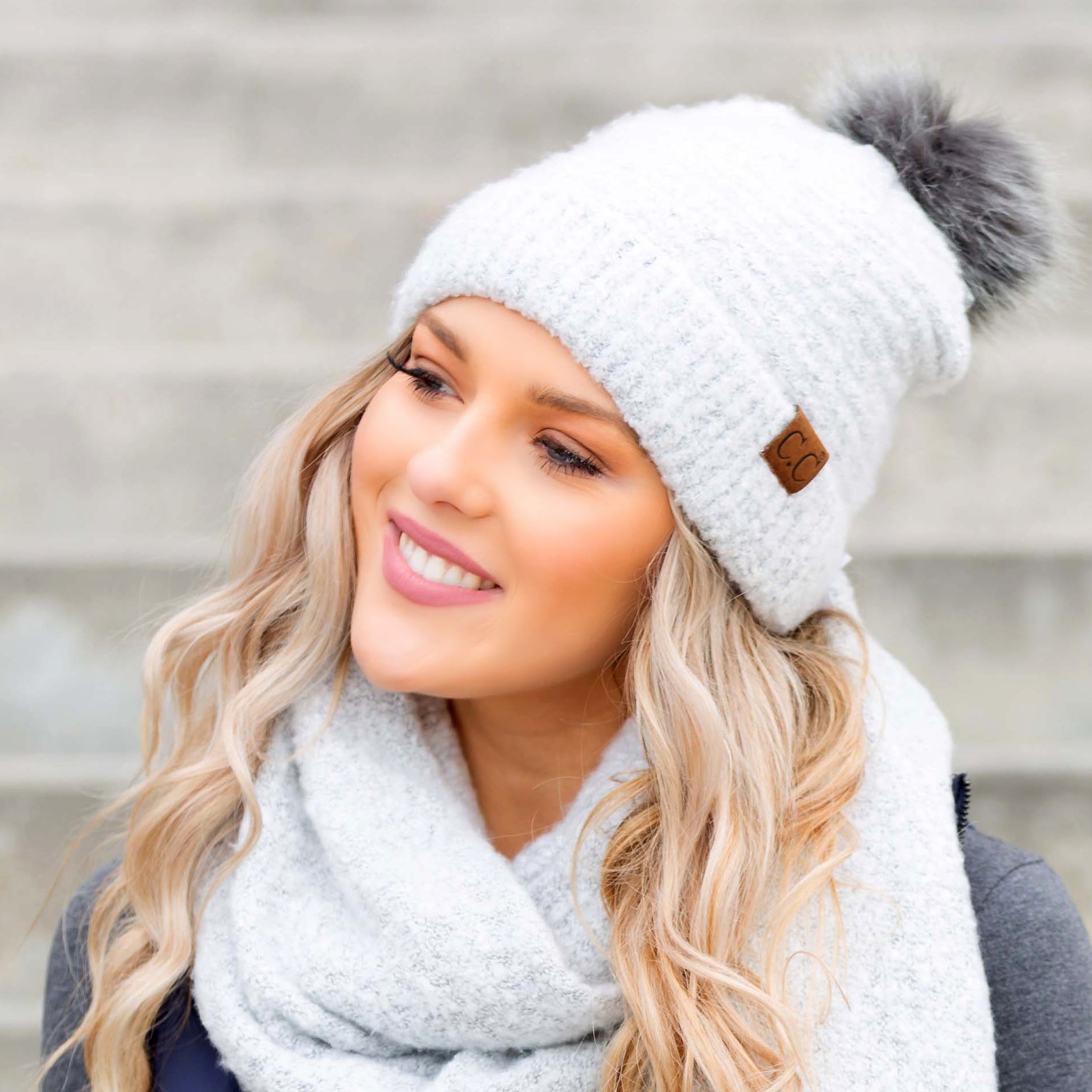 White boucle knit hat with faux fur pom worn with scarf, angled view