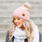 Blush boucle knit hat with faux fur pom worn with scarf, angled view