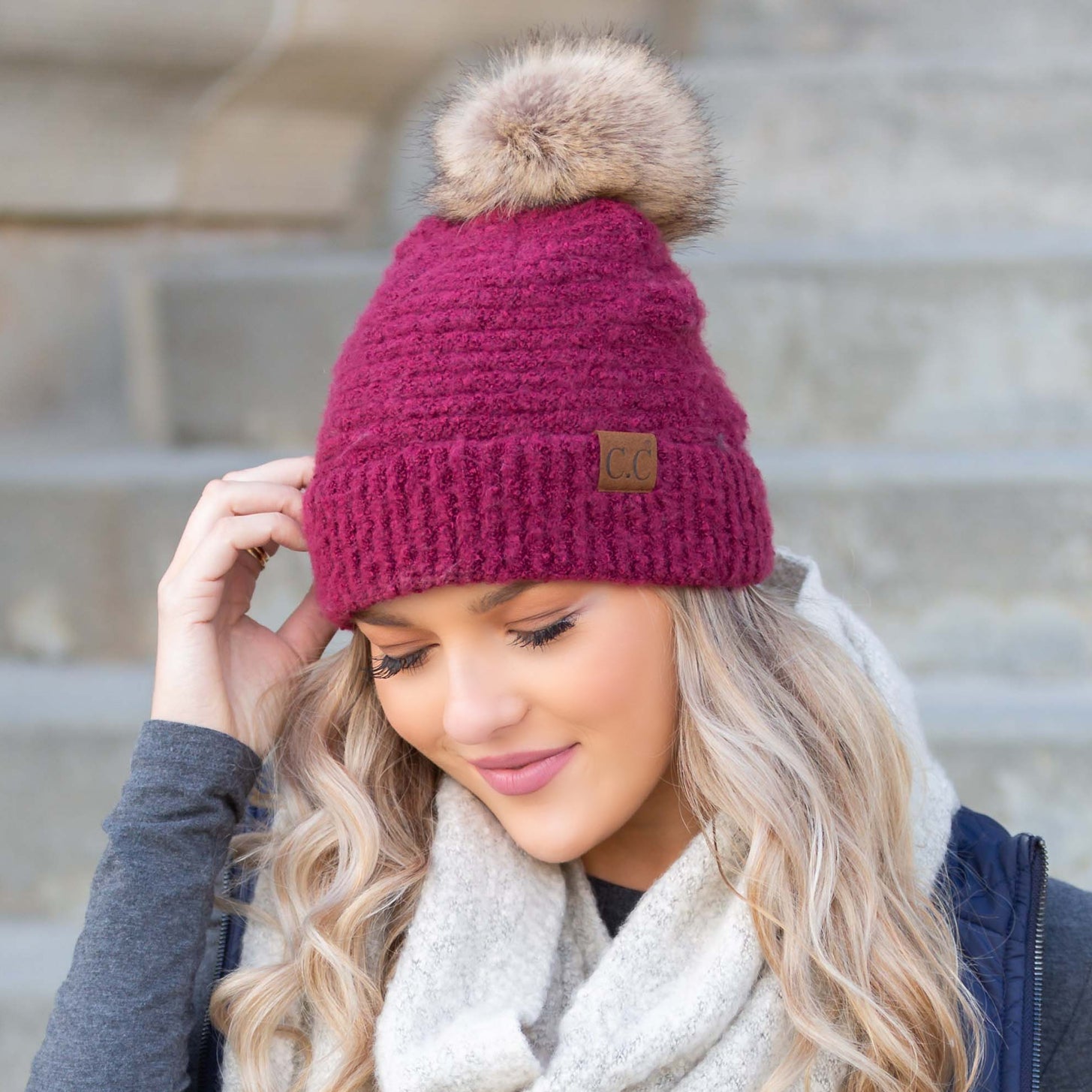 Pink boucle knit hat with faux fur pom worn with scarf, angled view