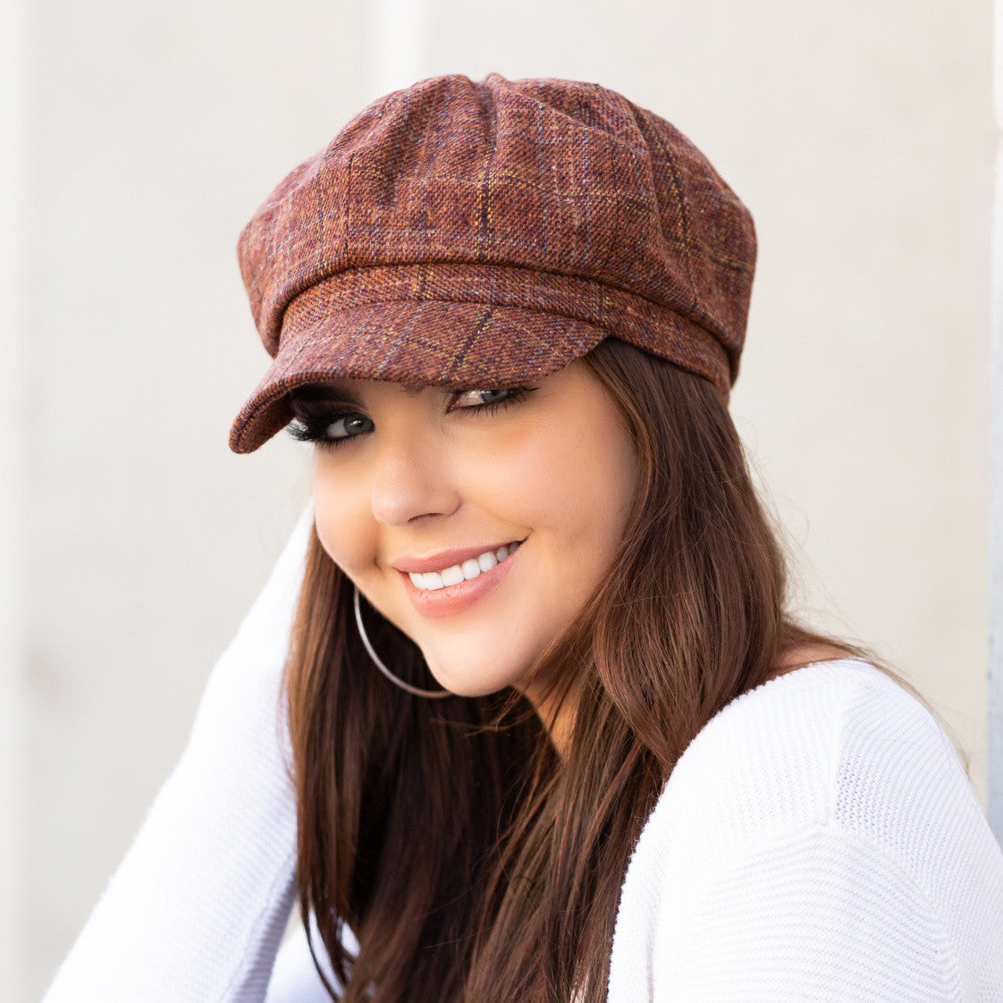 Woman wearing a rust tweed baker boy cap with a structured brim, side view against a pale wall