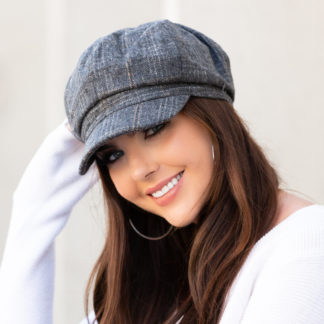 Woman wearing a gray tweed baker boy cap with a structured brim, side view against a pale wall