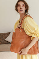 Woman holding a tan leather tote bag in a casual setting