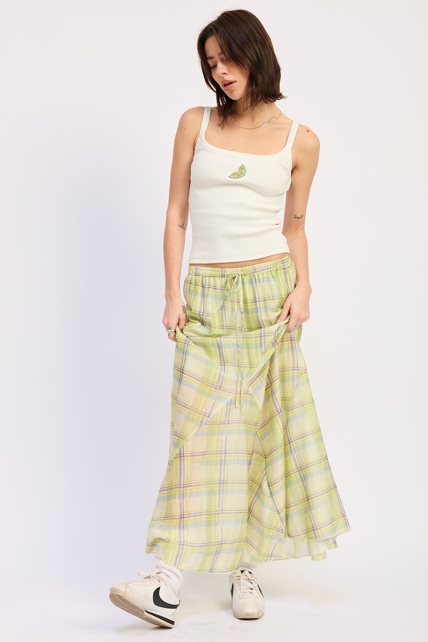 Woman wearing a white tank top and lime green plaid skirt on a white background