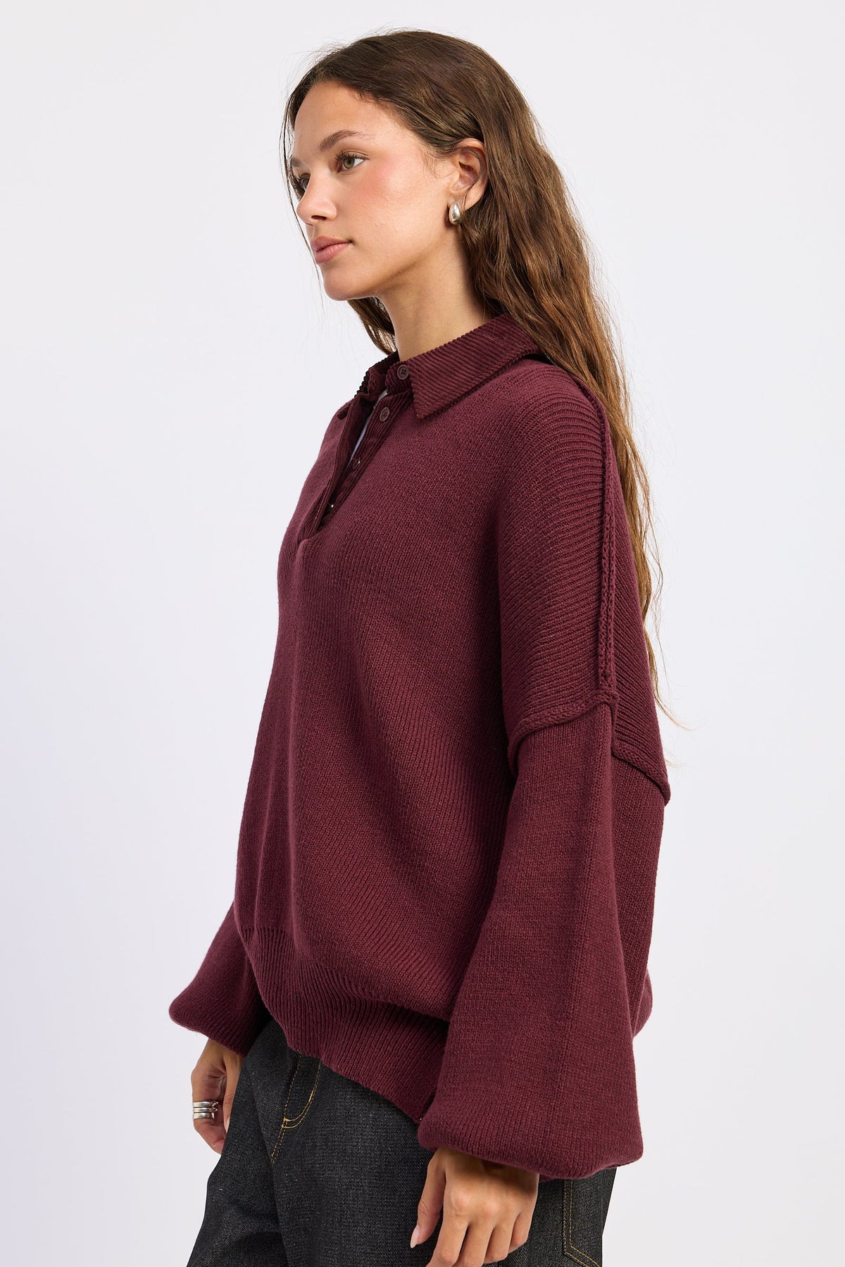 Side view of burgundy collared knit sweater showing dropped shoulders, exposed seams and voluminous sleeves.