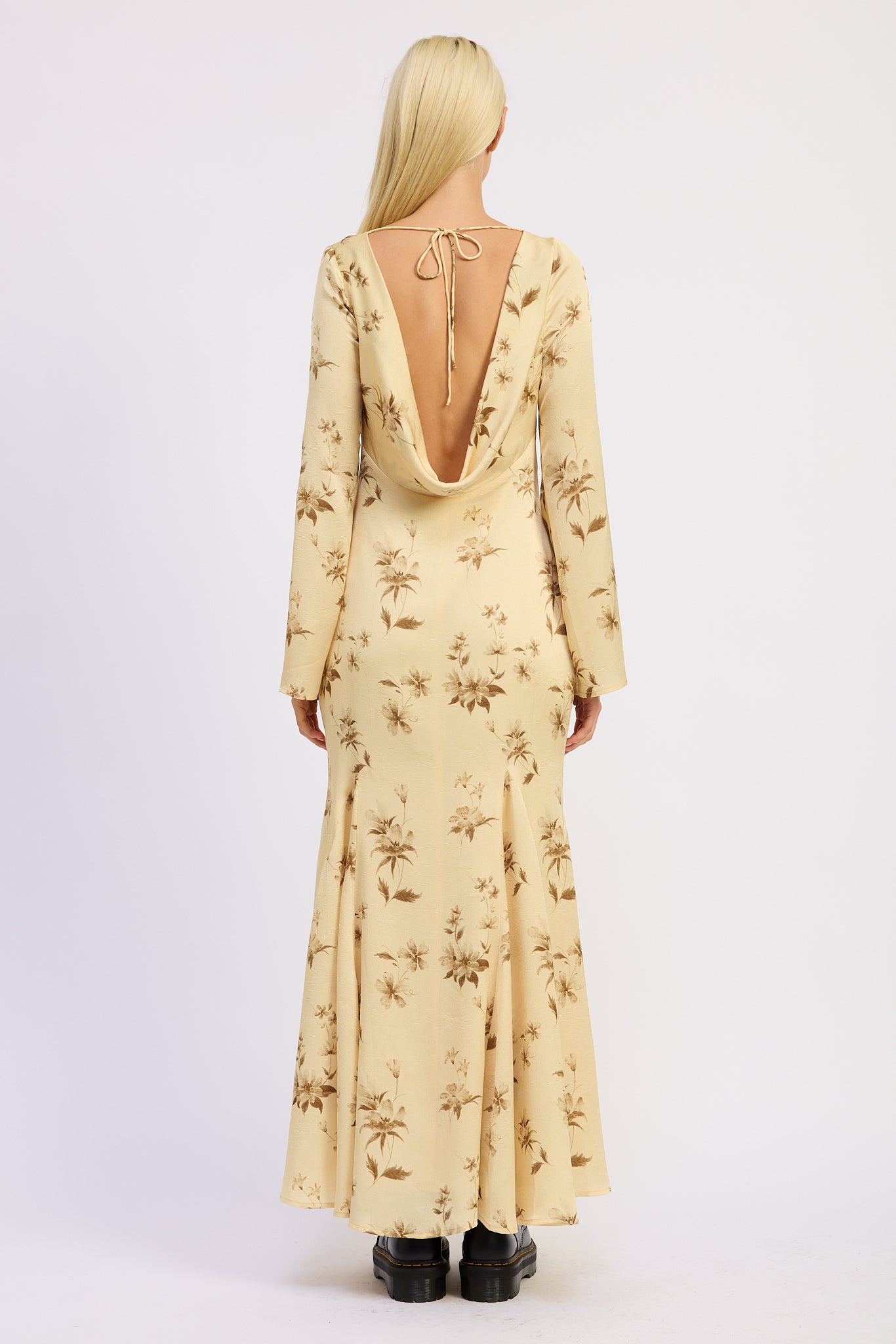 Woman wearing a long-sleeve, floral-patterned maxi dress with open back on a white background
