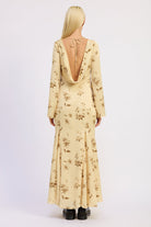 Woman wearing a long-sleeve, floral-patterned maxi dress with open back on a white background