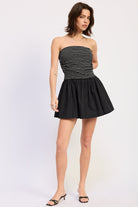 Woman wearing a black strapless mini dress striped bodice contrast skirt on a white background 