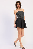 Woman wearing a black strapless mini dress striped bodice contrast skirt on a white background 