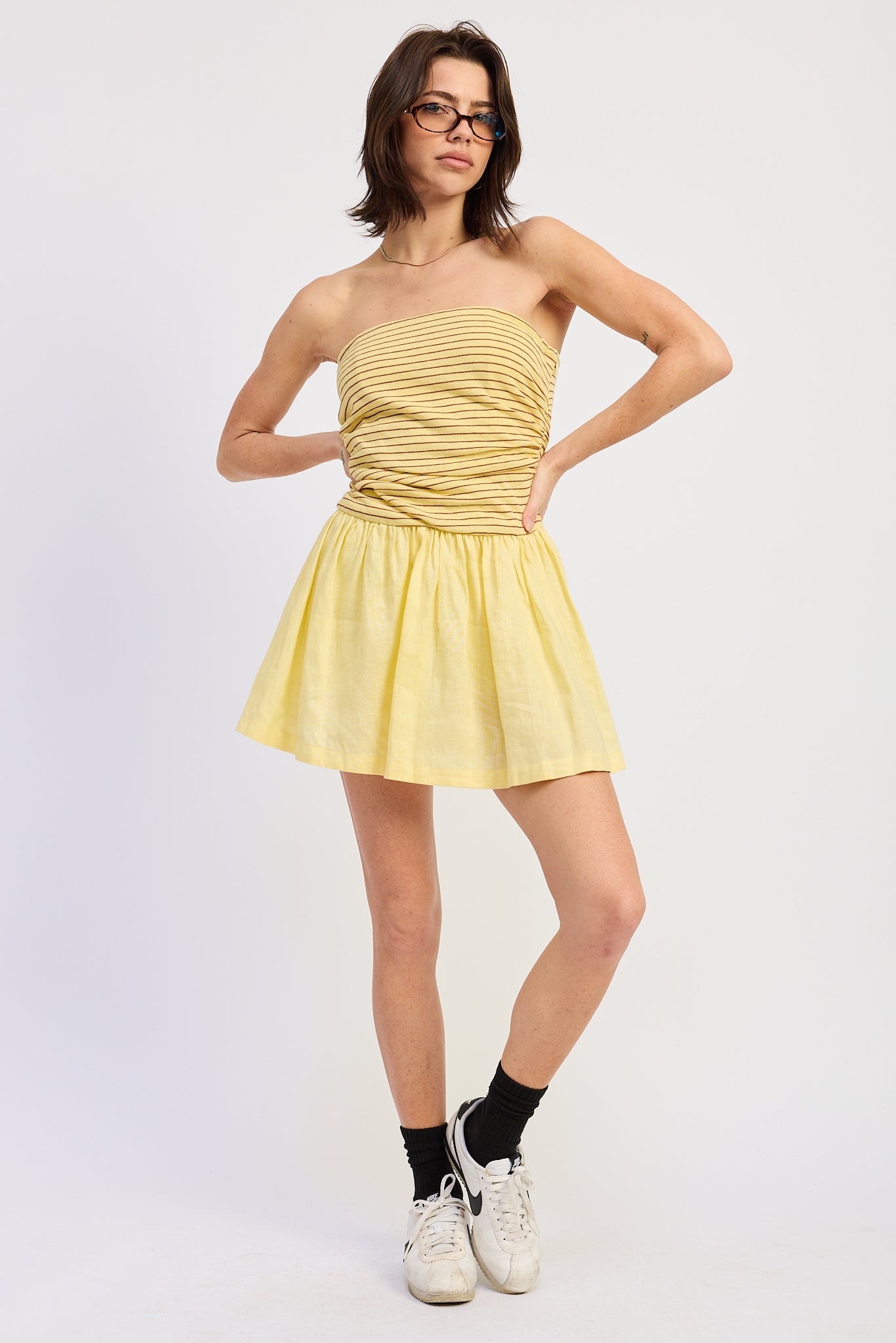 Woman wearing a yellow strapless mini dress striped bodice contrast skirt on a white background 