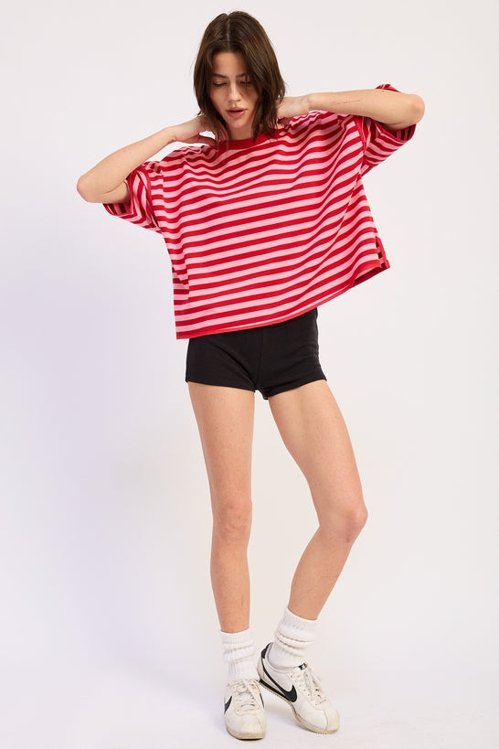 Woman wearing a red and pink striped shirt with light blue jeans on a plain background