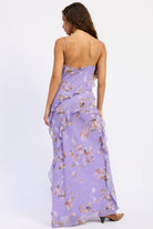 Back view of lavender floral ruffle maxi dress with cowl neckline, spaghetti straps, cascading ruffles and front slit.
