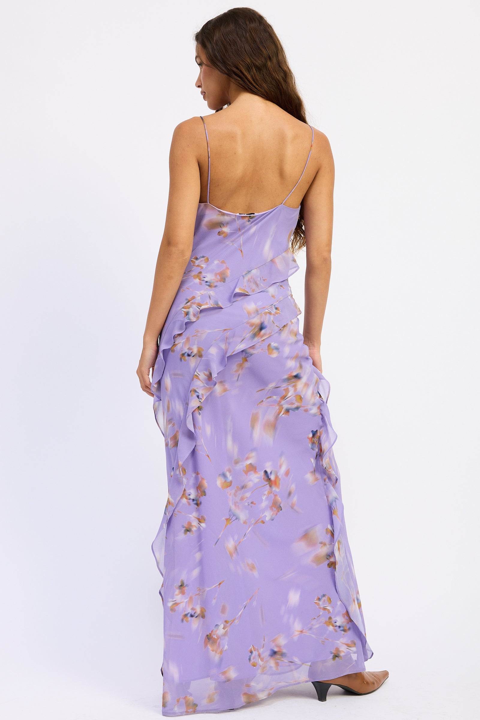 Back view of lavender floral ruffle maxi dress with cowl neckline, spaghetti straps, cascading ruffles and front slit.
