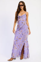Woman wearing a lavender floral ruffle maxi dress with cowl neckline, spaghetti straps, cascading ruffles and front slit.
