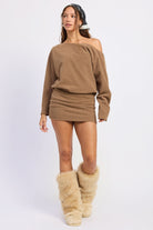 Woman wearing brown long-sleeve mini dress with tall textured boots against white background.