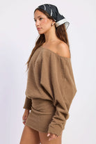 Woman wearing brown off-shoulder mini dress with draped long sleeves, side view against white background.