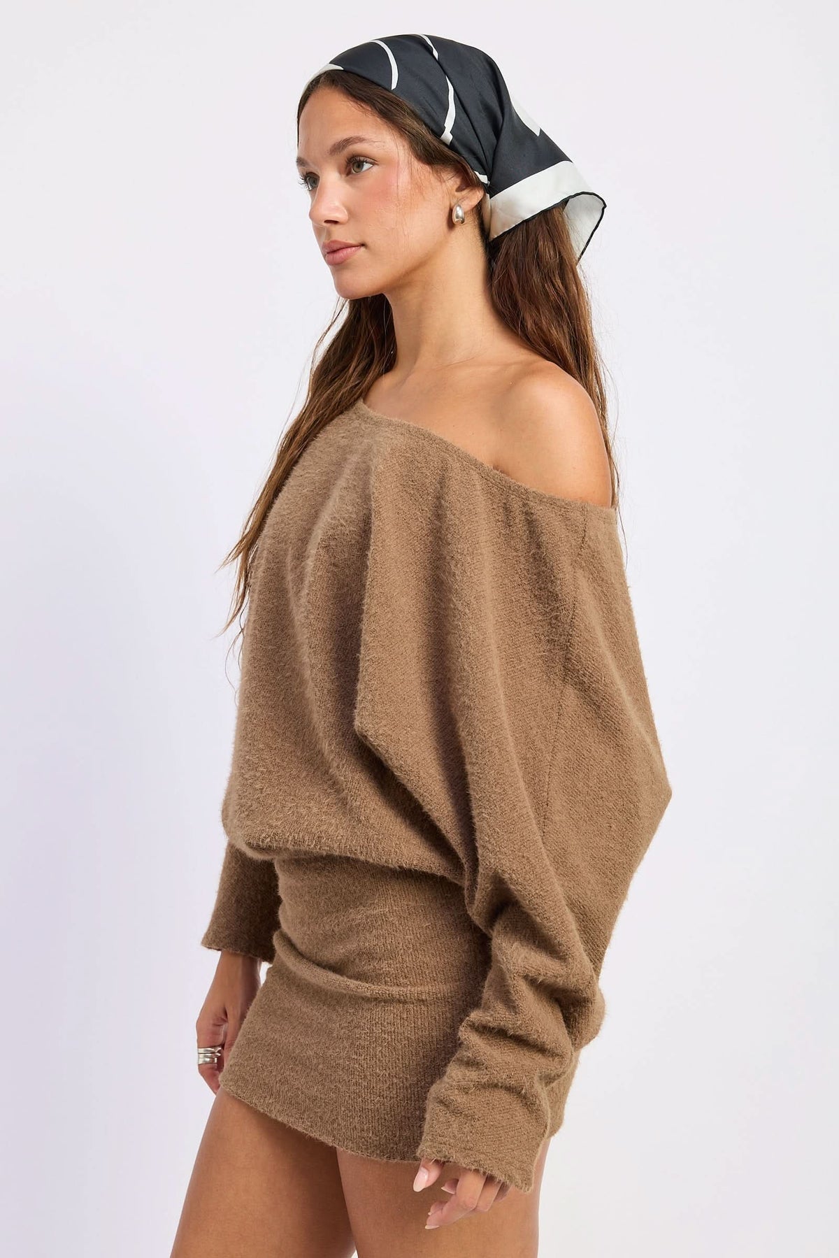 Woman wearing brown off-shoulder mini dress with draped long sleeves, side view against white background.