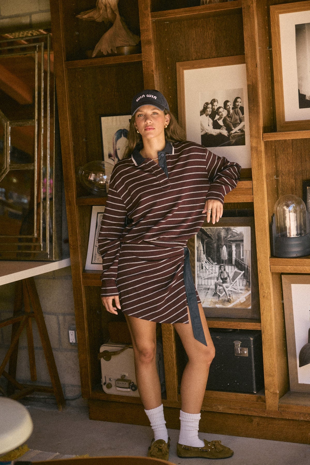 Model wearing burgundy Varsity Club Striped Polo Mini Dress with navy collar, wrap-style skirt and side tie in a vintage-inspired interior.