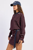 Side view of burgundy striped rugby mini dress showing dropped shoulders, button cuffs and navy side tie.