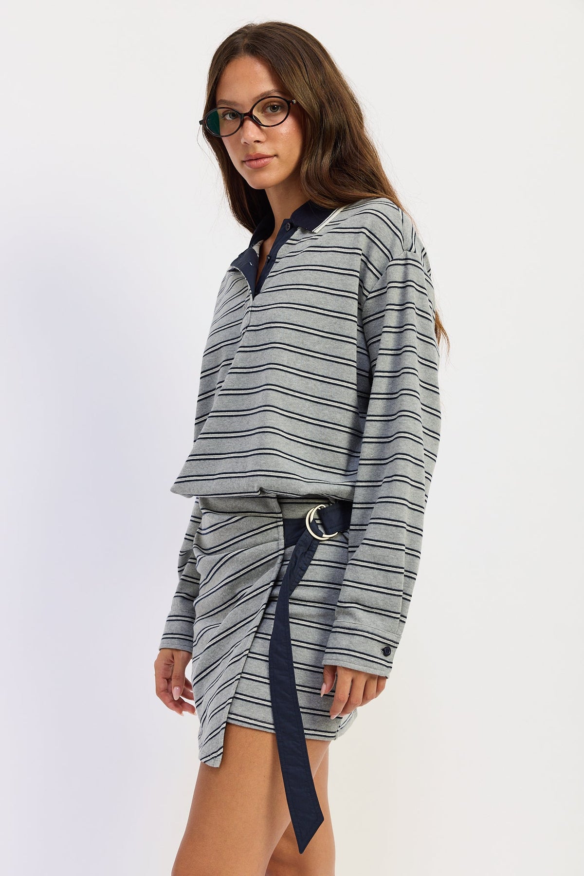 Angled view of heather grey striped polo mini dress showing navy side tie, long sleeves and asymmetrical skirt.