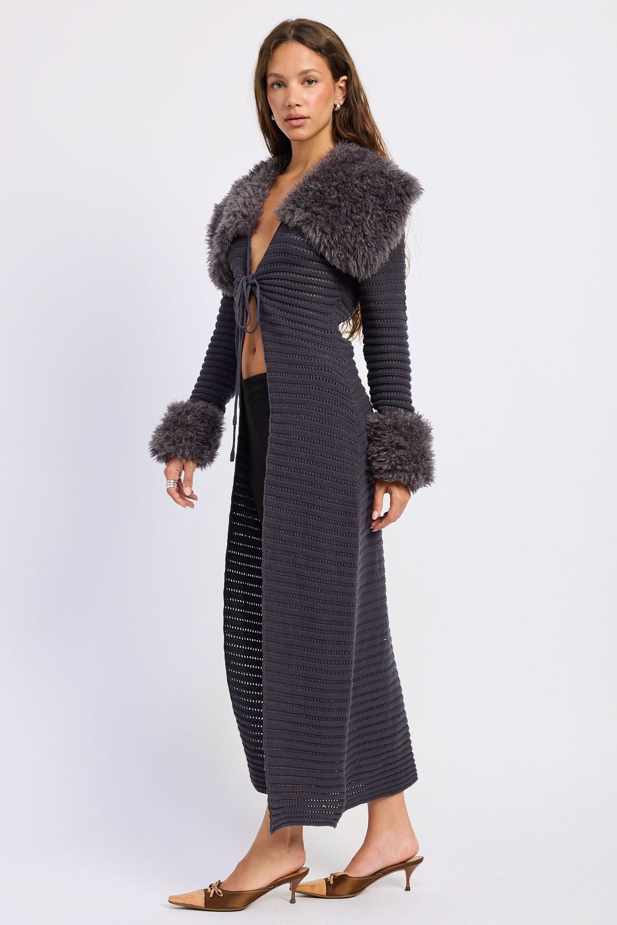 Woman wearing grey midi cardigan, side view showing open knit texture and plush trim against white background.