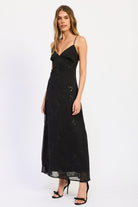 Woman wearing black V-neck maxi dress with delicate straps and floral detail.
