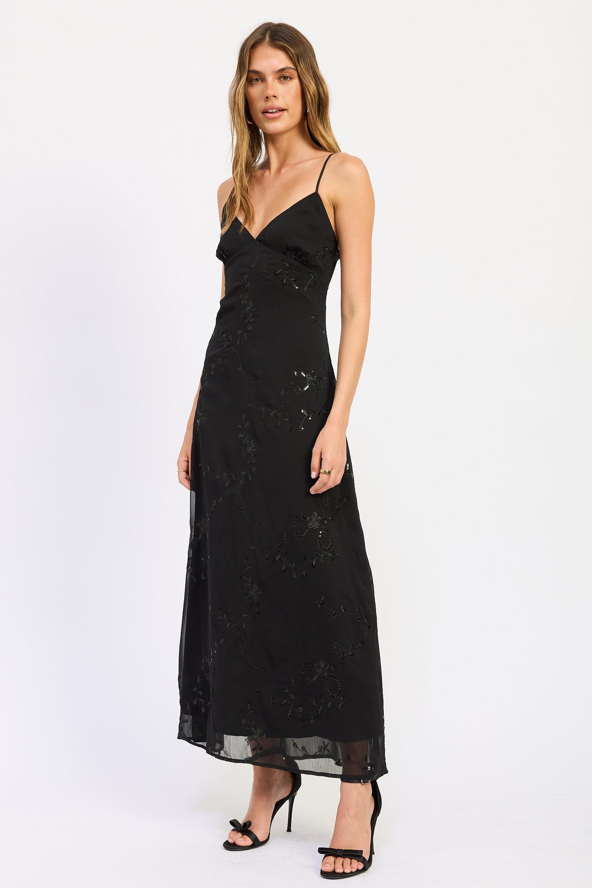 Woman wearing black V-neck maxi dress with delicate straps and floral detail.
