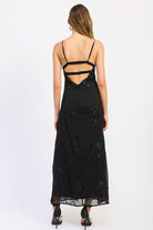 Woman wearing black V-neck maxi dress with delicate straps and floral detail.