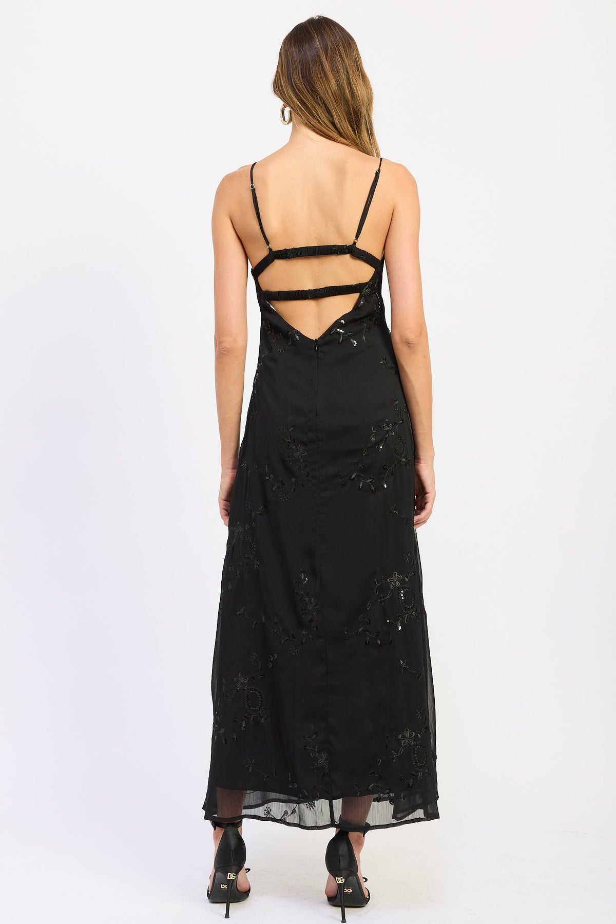 Woman wearing black V-neck maxi dress with delicate straps and floral detail.