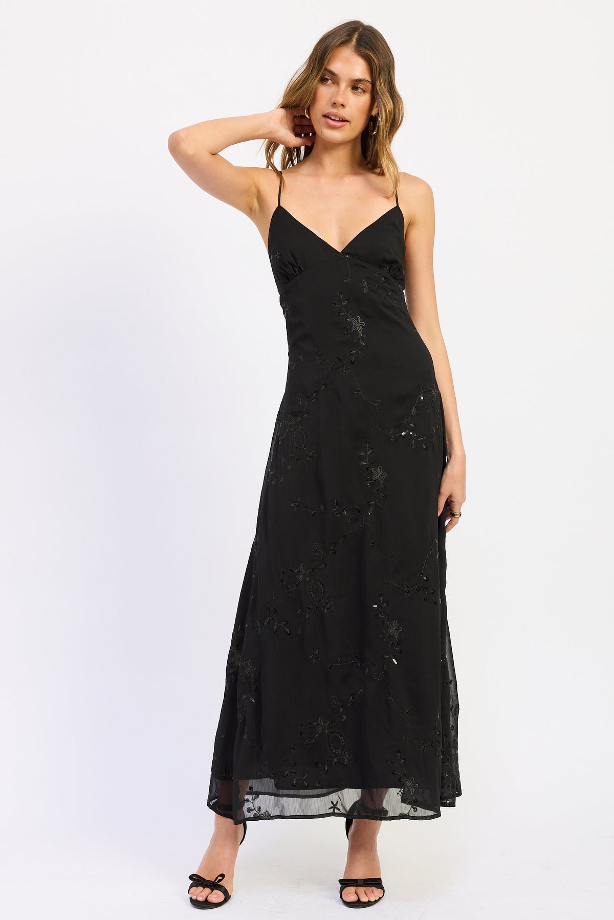 Woman wearing black V-neck maxi dress with delicate straps and floral detail.
