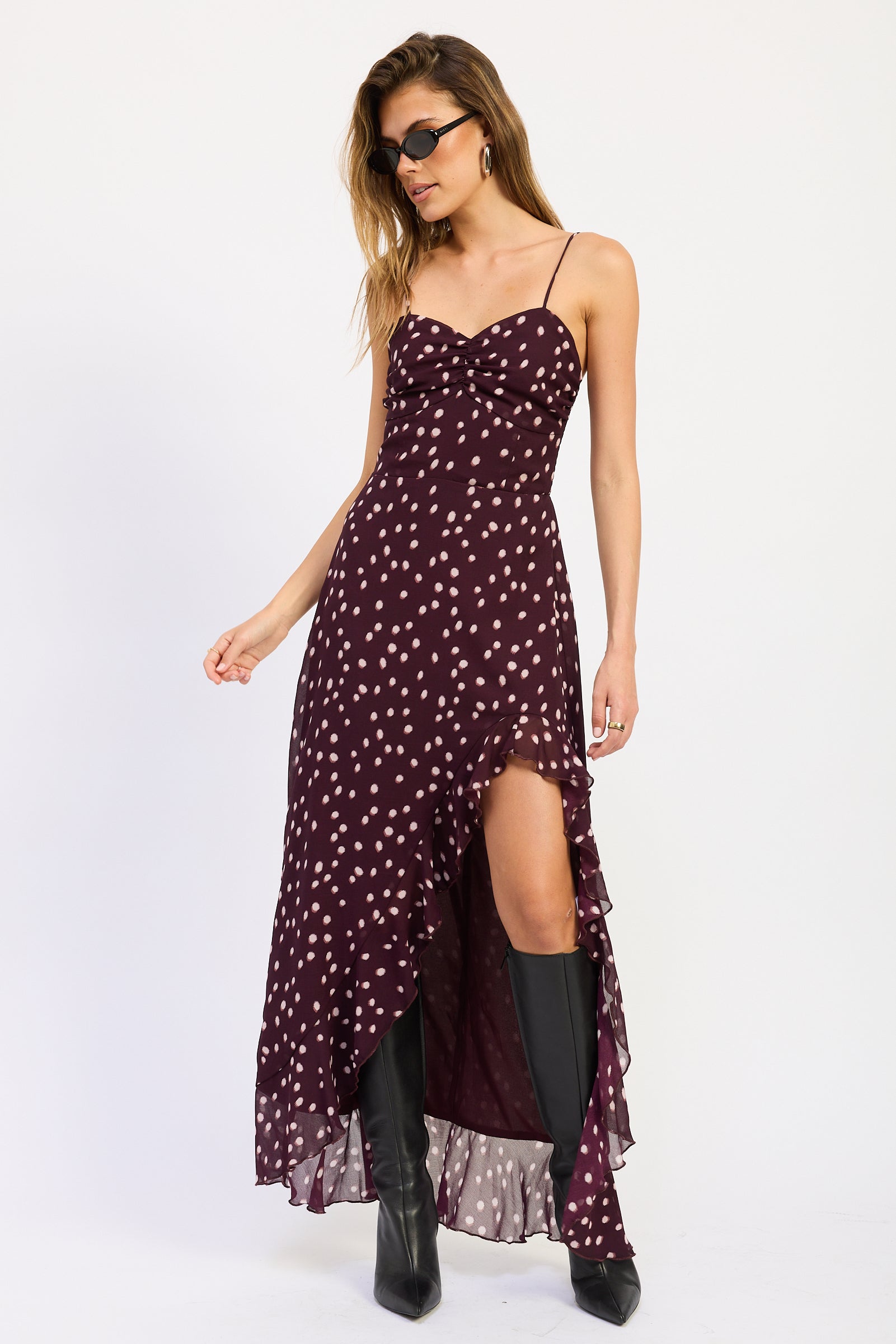 Woman wearing polka dot maxi dress with spaghetti straps and ruffled asymmetric hem in Wine.