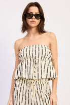 Woman wearing a Strapless cream and black striped peplum top with matching pants on a white background front view