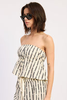 Woman wearing a Strapless cream and black striped peplum top with matching pants on a white background front angle view