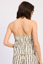 Woman wearing a Strapless cream and black striped peplum top with matching pants on a white background back view